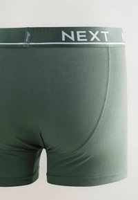 Boxers en tissu vert foncé pour homme, avec une taille douce portant l'inscription "NEXT" en blanc, texture douce et coupe ajustée.