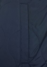 Tessuto trapuntato navy che mostra una texture liscia, con cuciture visibili e un dettaglio a ciclo rettangolare. Il design presenta motivi arrotondati.