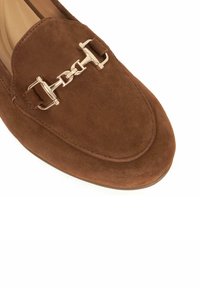 Brown suede loafer with a rounded toe, featuring gold-tone hardware accents, a chain detail on the vamp, and a smooth interior lining.