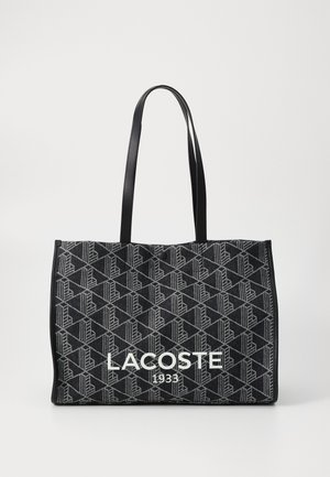 Duża prostokątna torba tote w czarnym materiale z geometrycznym wzorem. Zawiera dwie solidne czarne uchwyty oraz białe logo "LACOSTE 1933".