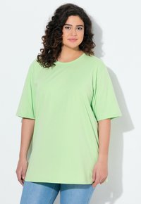 Grünes übergroßes T-Shirt aus weichem Stoff mit kurzen Ärmeln, rundem Ausschnitt und lockerer Passform. Getragen mit hellblauen Jeans.