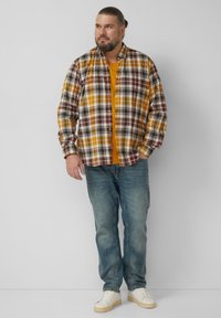 Geruit overhemd met bordeauxrood, geel en wit; gecombineerd met een oranje ondershirt. Draagbaar met een lichtblauwe spijkerbroek en witte sneakers.