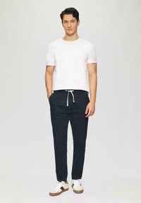 Witte kortekrijtshirt gecombineerd met marineblauwe joggingsbroeken met een elastische tailleband en trekkoord. Model draagt witte sneakers.