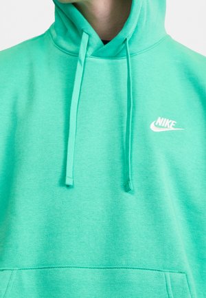 Turkusowa bluza z kapturem Nike z troczkami i białym logo Nike po lewej stronie na piersi, noszona przez niewidoczną osobę.