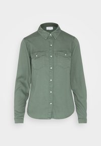 Vihreä puuvillapaita, jossa on teräväkauluksellinen design, napitus edessä, kaksi rintataskua ja pitkät hihat. Ominaisuuksina pehmeä, teksturoitu pinta.