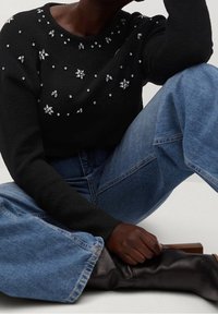 Pull noir orné de décorations, avec un col rond et des manches longues. Associé à un jean en denim bleu taille haute.