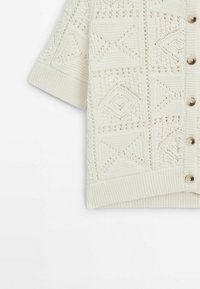 Short-sleeved cream cardigan with textured knitted pattern, featuring diamond shapes, large buttons, and a ribbed hem and cuffs.