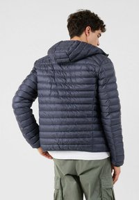 Doudoune bleu marine avec coutures horizontales, capuche et poignets élastiques. Matériau léger avec une texture légèrement brillante visible à la surface.