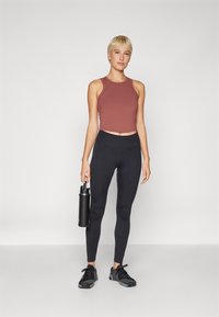 Maroon cropped tank top, black high-waisted leggings, holding a black water bottle, paired with black athletic shoes. Smooth fabric texture.