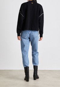 Černý zkrácený svetr s lemy na rukávech, kombinovaný se světle modrými džínami s vysokým pasem a černými kozačkami na podpatku sahajícími nad kolena.