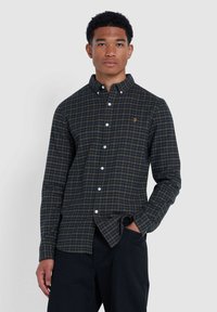 Chemise à manches longues à carreaux bleu marine et vert avec col boutonné, dotée de boutons blancs et d'un petit logo brodé sur la poitrine.