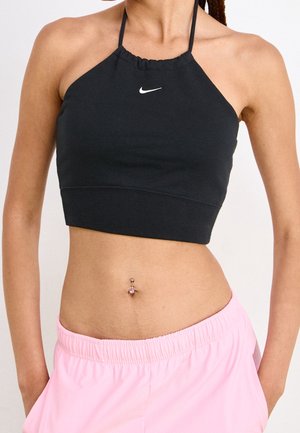 Femme portant un crop top noir Nike à bretelles et un pantalon rose clair à taille élastique, avec un piercing visible au nombril.