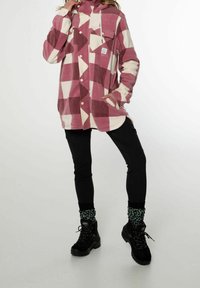 Camicia in pile a scacchi rosa e crema con cappuccio, tasca frontale e bottoni, abbinata a pantaloni neri e stivali neri con calze verdi a fantasia.