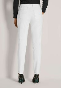 Witte strakke broek met een elastische tailleband en twee achterzakken, gecombineerd met zwarte hoge hakken en een gestructureerde zwarte top.