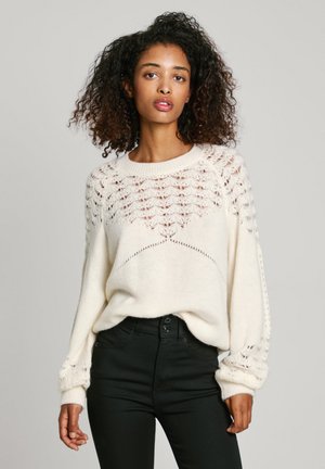 Crème trui met een getextureerd kantpatroon over de schouderpartij en oversized mouwen. Gecombineerd met zwarte slim-fit spijkerbroek.