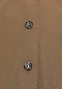 Brown fabric with two round black and grey marbled buttons sewn vertically along a stitched seam.