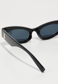 Occhiali da sole a forma di gatto con una montatura nera lucida, lenti scure e un accentuazione dorata sulla tempia, caratterizzati da linee di design slanciate ed eleganti.