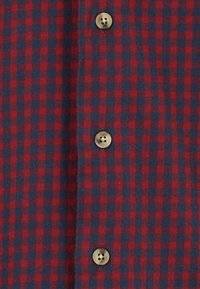 Czerwona i granatowa flanelowa koszula w kratę z dużymi, okrągłymi, beżowymi guzikami z przodu, charakteryzująca się miękką fakturą i spójnym wzorem.