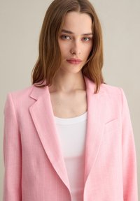 Blazer rosa chiaro con motivo a righe, chiusura a singolo petto, rever a punta e una sottile texture, abbinato a una canotta bianca.