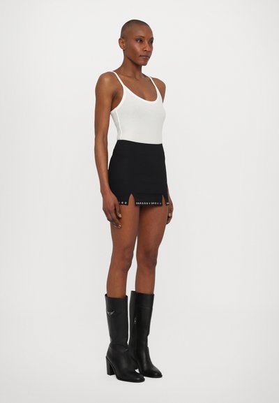 Λευκό κορμάκι, εφαρμοστή μαύρη μίνι φούστα με μπροστινές σχισμές και ασημένια μεταλλικά στοιχεία, συνδυασμένη με μαύρες ψηλές μπότες. Λείες υφές σε όλη την επιφάνεια.