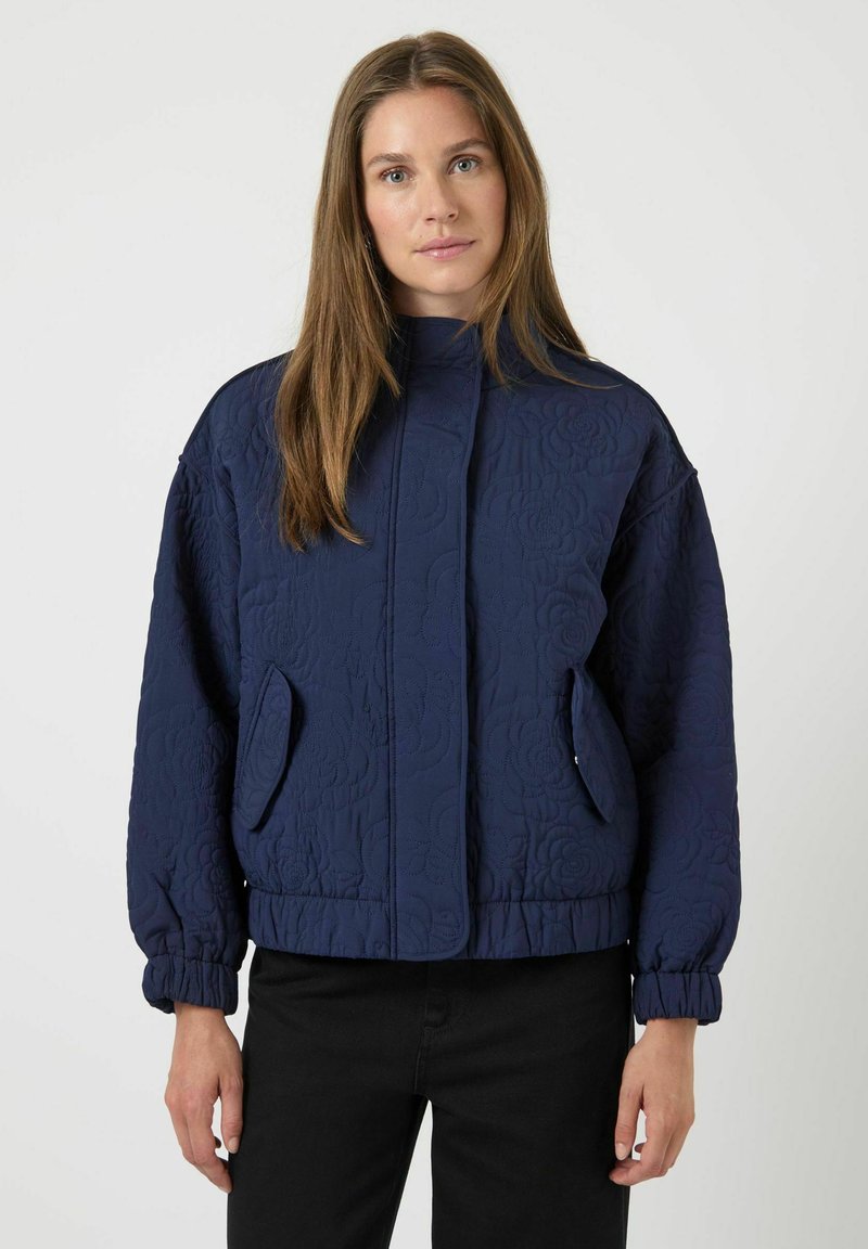 Marinblå quiltad jacka med hög krage, elastiska ärmslut och två sidofickor. Strukturerat blommönster ger detalj.