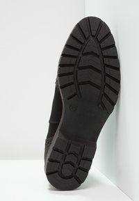 Semelle de chaussure noire avec un design texturé et adhérent. Présente une tige noire lisse et des découpes complexes le long du bord.