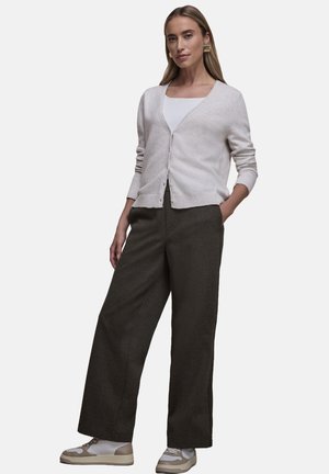 Světlý béžový kardigan s výstřihem do V a zapínáním na knoflíky, v kombinaci s tmavými širokými kalhotami a bílými teniskami s béžovými detaily.