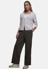 Jasnobeżowy kardigan z dekoltem w serek i zapięciem na guziki, w połączeniu z szerokimi ciemnymi spodniami i białymi trampkami z beżowymi akcentami.