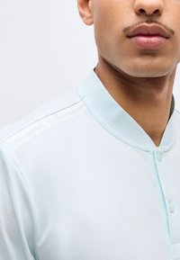 Κοντινό πλάνο ενός ατόμου που φορά ανοιχτό μπλε πουκάμισο με κουμπιά και λευκές διακοσμητικές ρίγες στον ώμο.