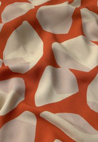 Abstrakter Stoff mit großen, unregelmäßigen cremefarbenen Formen auf einem kräftig orangefarbenen Hintergrund. Die Oberfläche hat eine glatte Textur mit einem leichten Glanz.