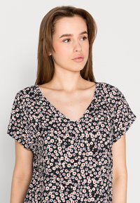 Blusa preta com flores, com mangas curtas, decote em V, e um padrão de pequenas flores cor-de-rosa e brancas com detalhes verdes.