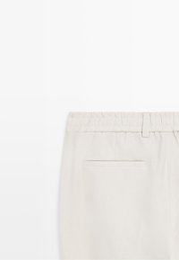 Light beige pants with elastic waistband and single welt back pocket, shown from the backside on a white background.