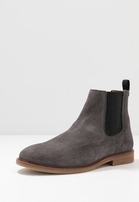 Stivaletto Chelsea grigio in suede con pannelli elastici laterali e suola in legno marrone. Presenta un piccolo passante sul retro e un discreto logo inciso.