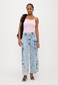 Lys rosa tank topp, høyt liv, vide lys denimjeans med flere cargo-lommer, teksturert stoff og svarte stroppehæler.
