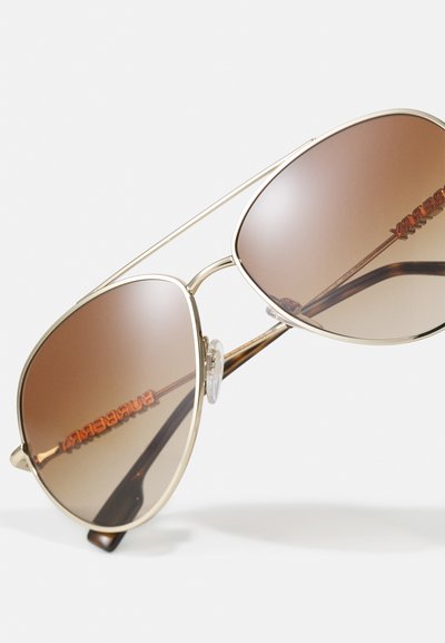 Occhiali da sole aviator in metallo dorato con lenti marroni sfumate, dotati di cuscinetti per il naso trasparenti e marchio arancione lungo la lente.