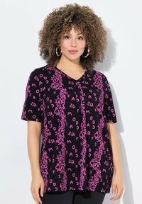 Camiseta negra de manga corta con escote en V, adornada con letras rosas en diferentes orientaciones, creando un patrón dinámico.