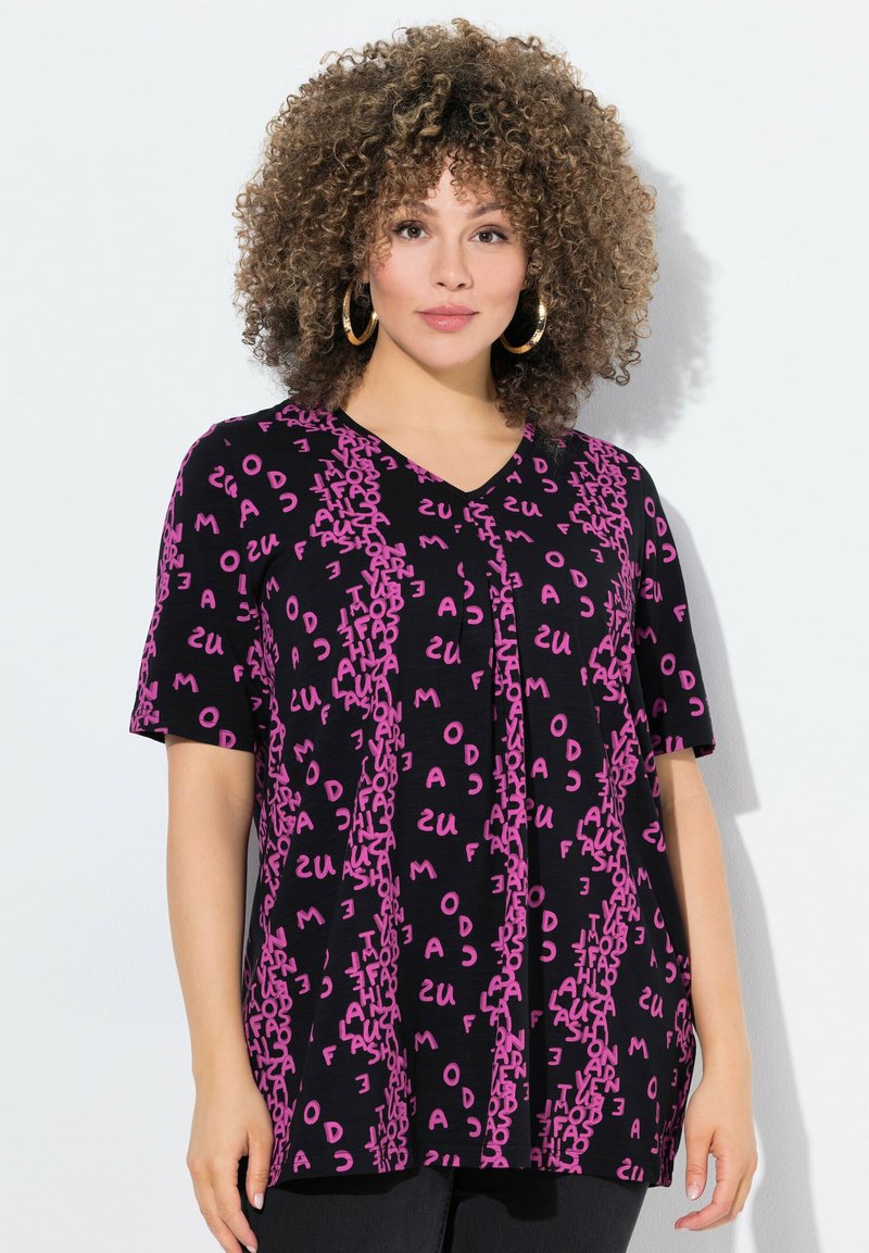 Camiseta negra de manga corta con escote en V, adornada con letras rosas en diferentes orientaciones, creando un patrón dinámico.