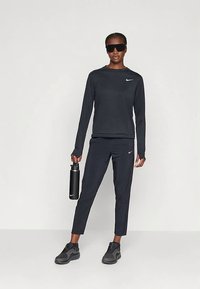 Fekete sportos összeállítás, amely hosszú ujjú felsőből és karcsúsított nadrágból áll, rugalmas anyagból készült. Kiegészítők között fekete vízpalack és napszemüveg található.