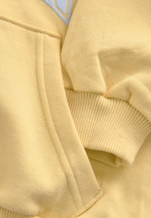 Yellow cotton sweatshirt featuring a kangaroo pocket, ribbed cuffs, and textured fabric. Accented with a white geometric design.