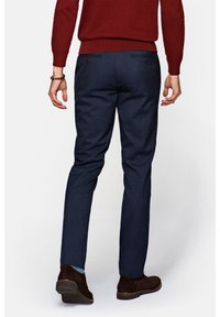 Granatowe spodnie z fakturowanej tkaniny, slim fit, z tylnymi kieszeniami. Noszone z brązowymi zamszowymi butami i czerwonym swetrem.