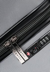 Zilveren ritssluiting met dubbele sliders, bevestigde labels met het merk "bugatti," tegen een gestructureerde zwarte stof. Inclusief een combinatielocksysteem.