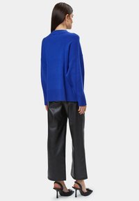 Maglione oversized blu royal, vestibilità rilassata, polsini a coste, abbinato a pantaloni in ecopelle neri a vita alta e mule nere con tacco.