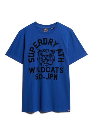 Blauw T-shirt met zwarte tekst "SUPERDRY ATH WILDCATS SD-JPN" en een grafiek van het hoofd van een brullende wilde kat, gecentreerd onder de kraag.