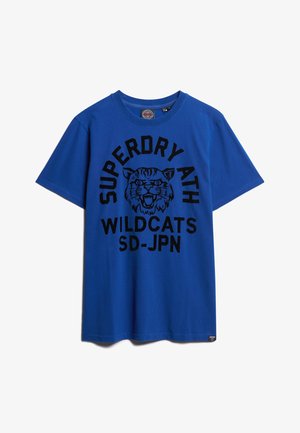 Blauw T-shirt met zwarte tekst "SUPERDRY ATH WILDCATS SD-JPN" en een grafiek van het hoofd van een brullende wilde kat, gecentreerd onder de kraag.