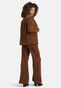 Brown corduroy suit with a tailored blazer and flared pants. The fabric features vertical ribs, and the blazer has front pockets.