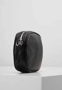 Borsa nera in pelle con superficie texturizzata, forma arrotondata e zip argentata. Dotata di una tracolla per il trasporto.