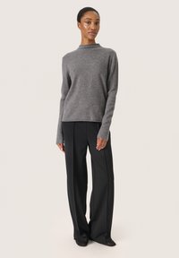 Grauer, langärmeliger Pullover mit hohem Kragen, kombiniert mit schwarzen, weit geschnittenen Hosen. Glatte Textur und minimalistisches Design sind auffällige Merkmale.