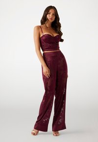 Costum format două piese de culoare burgundy, care include un top scurt din dantela florală, ajustabil pe umeri, și pantaloni evazați transparenți cu manșete solide.