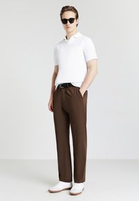 Polo bianco a maniche corte, pantaloni marroni, cintura nera e sneakers bianche. Gli occhiali da sole valorizzano l'outfit. Tessuto morbido, vestibilità su misura.