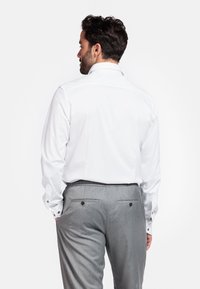 Witte langemouwen shirt met knoopmanchetten, gecombineerd met lichtgrijze broeken met achterzakken en een tailleband met elastiek.